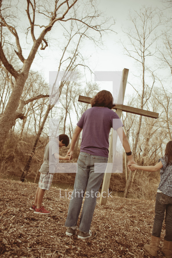 Mother and children holding hands before a wooden cross.