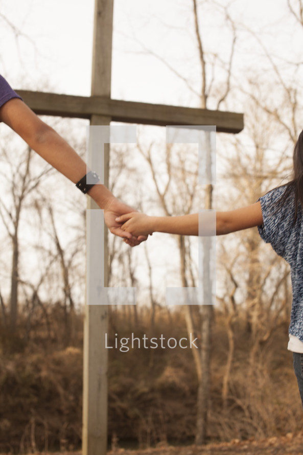 holding hands in prayer around a cross outdoors 