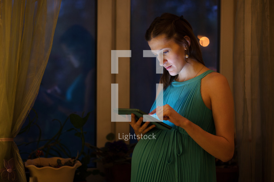 Pregnant woman using tablet in the evening