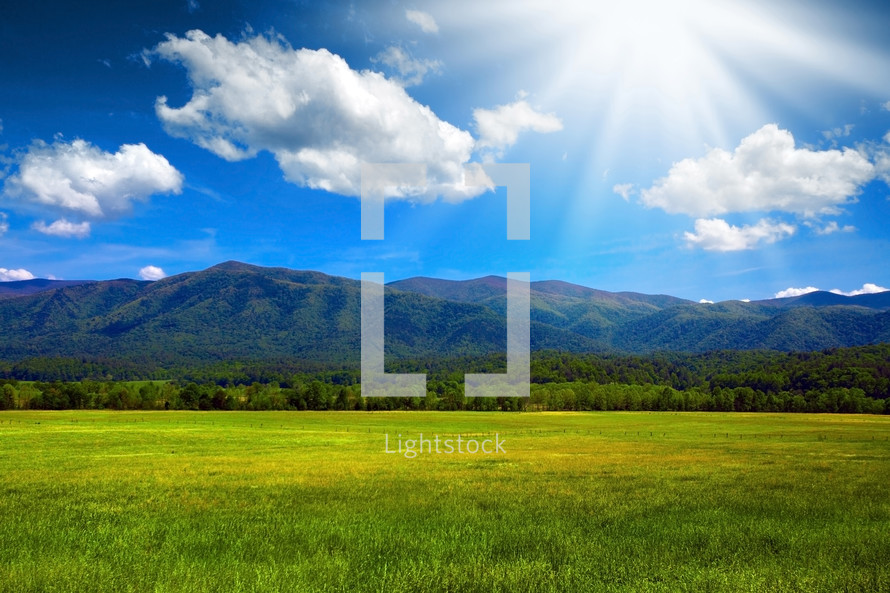 sunlight on a mountain behind an open grassy field 