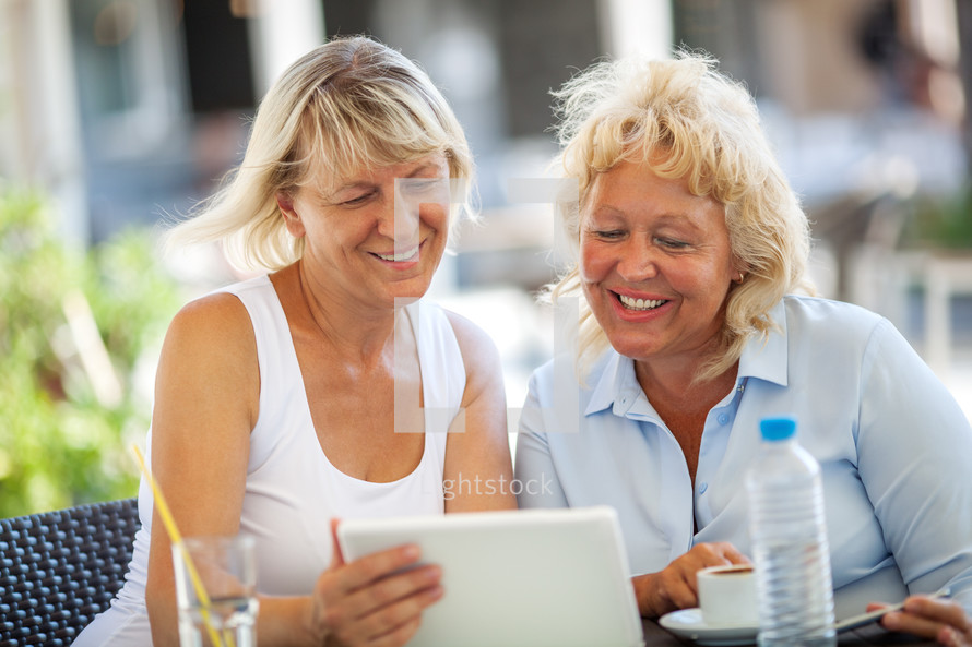 Two women friends using tablet PC in outdoor cafe