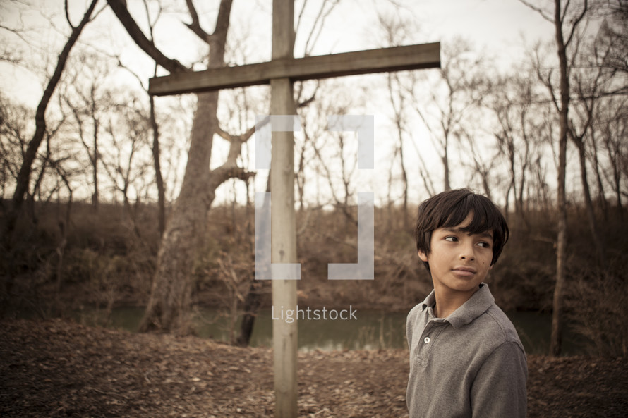 teen boy standing in front of a wood cross outdoors 