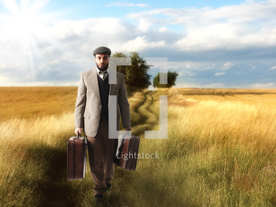 a man walking carrying luggage through a field 