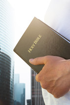 man holding a Bible standing in a city 