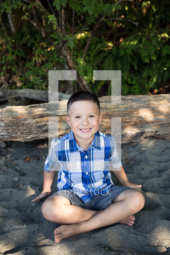 a boy smiling sitting in the sand 