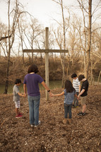 holding hands in prayer in front of a cross outdoors 