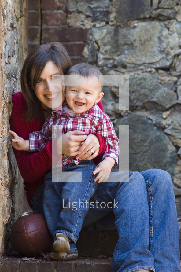 Mother holding toddler son while sitting on cement steps with football.