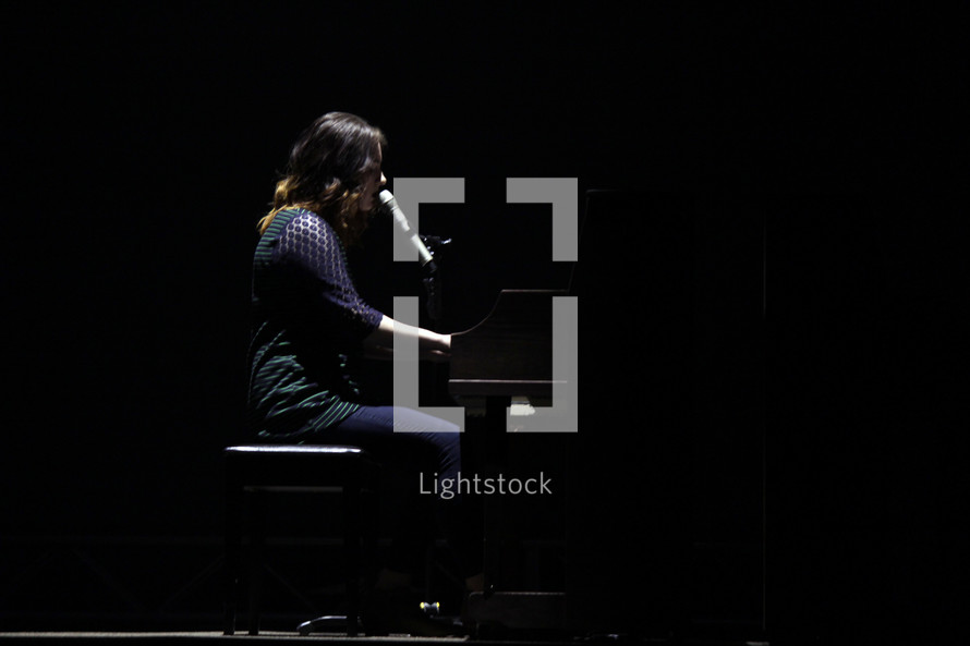 woman at a piano singing into a microphone on stage 
