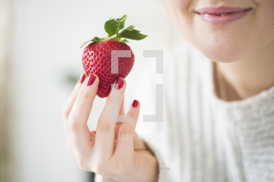 a woman holding a red strawberry 
