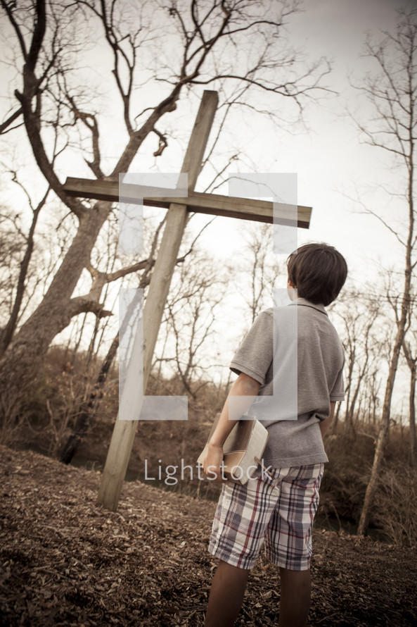 teen boy holding a Bible standing in front of a cross 