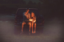 couple lighting sparklers on a tailgate 
