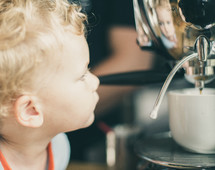 child looking at his reflection in a coffee maker 