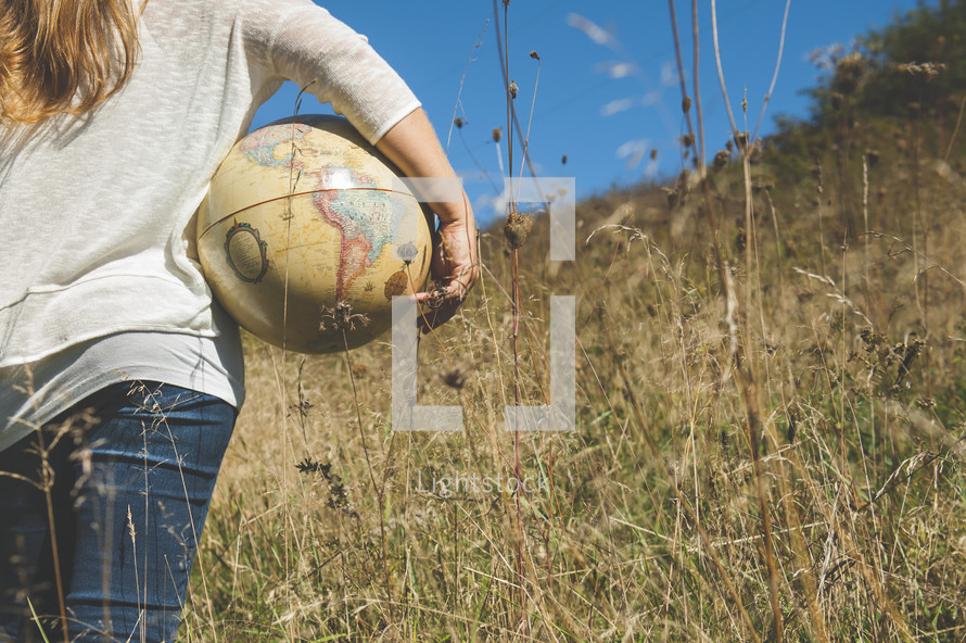 a woman standing outdoors in a field of tall grass holding a globe 