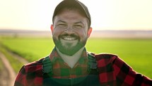 Portrait of a man with a beard working at a field. Farmer with a beard on the field. Portrait of a farmer. Cheerful male worker in agricultural farm. Sunlight. Agriculture farming.