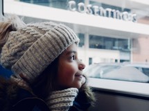 girl in a knit hat looking out a window 
