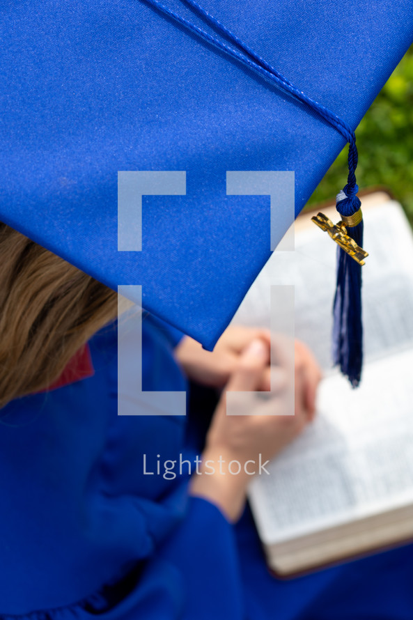 female graduate praying over a Bible 
