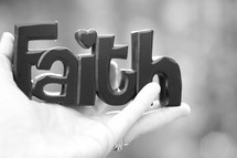 3D sign with the word faith, being held in a woman's hand