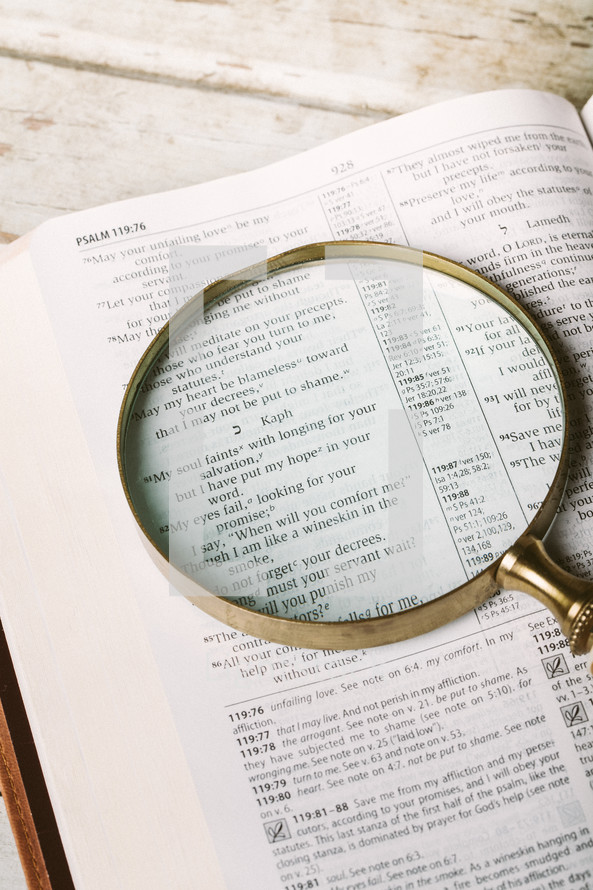 Magnifying glass on top of page of Bible open to Psalm 119:81 laying on wooden table.