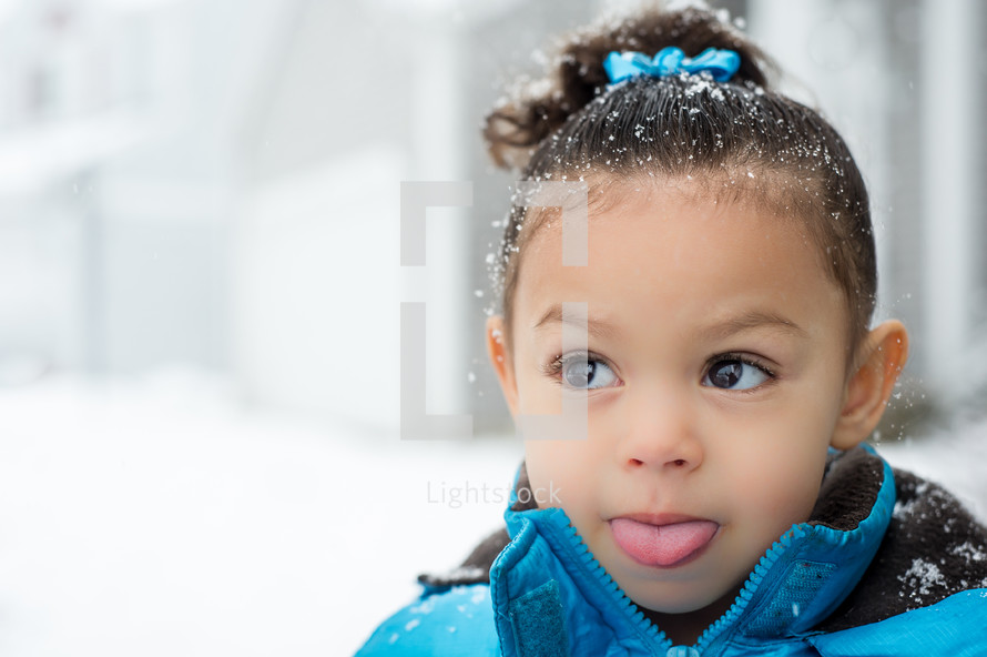 a toddler girl sticking out her tongue to catch snow flakes 