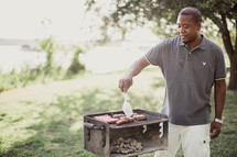 A man cooking hamburgers and hot dogs on an outdoor barbecue grill.