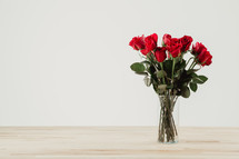 Red roses in a clear glass vase with a white background.