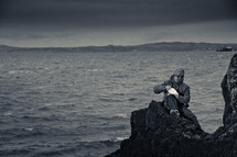 a man sitting on a rock along a shoreline 