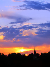 Vivid sunset silhouettes church steeple with cross.