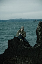 man journaling on a rock along a shoreline 
