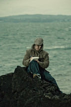man journaling on a rock on a beach 
