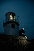 man sitting beneath a lighthouse at night 
