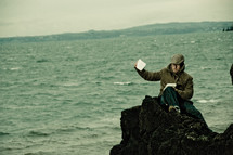 man sitting on a rock along a shoreline 