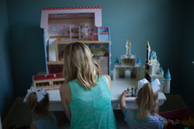a mother playing dollhouse with her daughters 