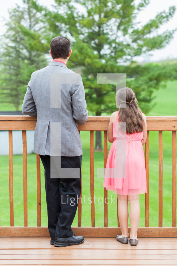 a father and daughter looking over a railing on a porch 