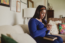 African-American woman reading a Bible and praying on the couch 