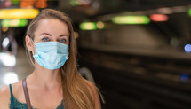 a young woman wearing a surgical mask standing in a subway 