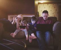 a family sitting on a couch playing electronics 
