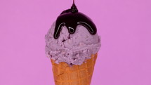 Lavender ice-cream in waffle cone rotating on pink background and liquid chocolate sauce pouring on it. Delicious isolated sweet dessert in studio