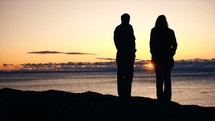 silhouettes of people standing on a beach at sunset 