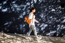 a woman walking on sidewalk carrying a backpack purse 