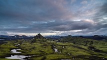 Sunset colors in sky clouds over green Icelandic mountains nature. Zoom in tilt up
