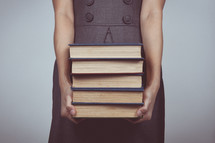 a woman in a dress holding a stack of books 