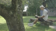 Young man opening up a journal outside on a bench.