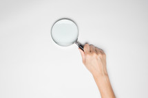 a hand holding a magnifying glass 