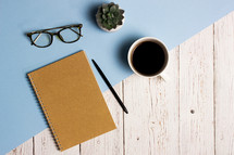 Working items with notebook, pencil, coffee cup and cactus over the blue and wooden background.  