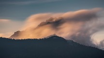 Fast misty clouds motion over alpine rocky peak in magic evening sunset light, long exposure time lapse
