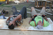 Two exhausted construction workers laying down on a plywood board.