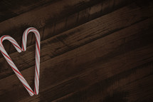 Two candy canes making the shape of a heart on wood