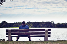 man sitting on a park bench looking out over a lake 