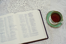 an open Bible and tea cup on a lace table cloth 