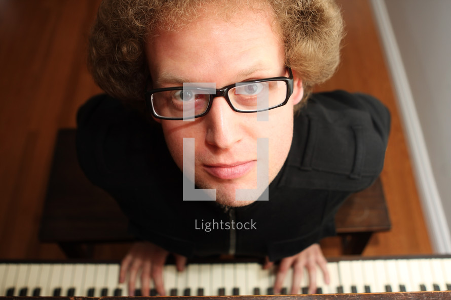 A man in glasses at a piano keyboard.